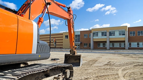 A bright orange construction excavator in the recently graded parking lot of a new high school.Similar Images: